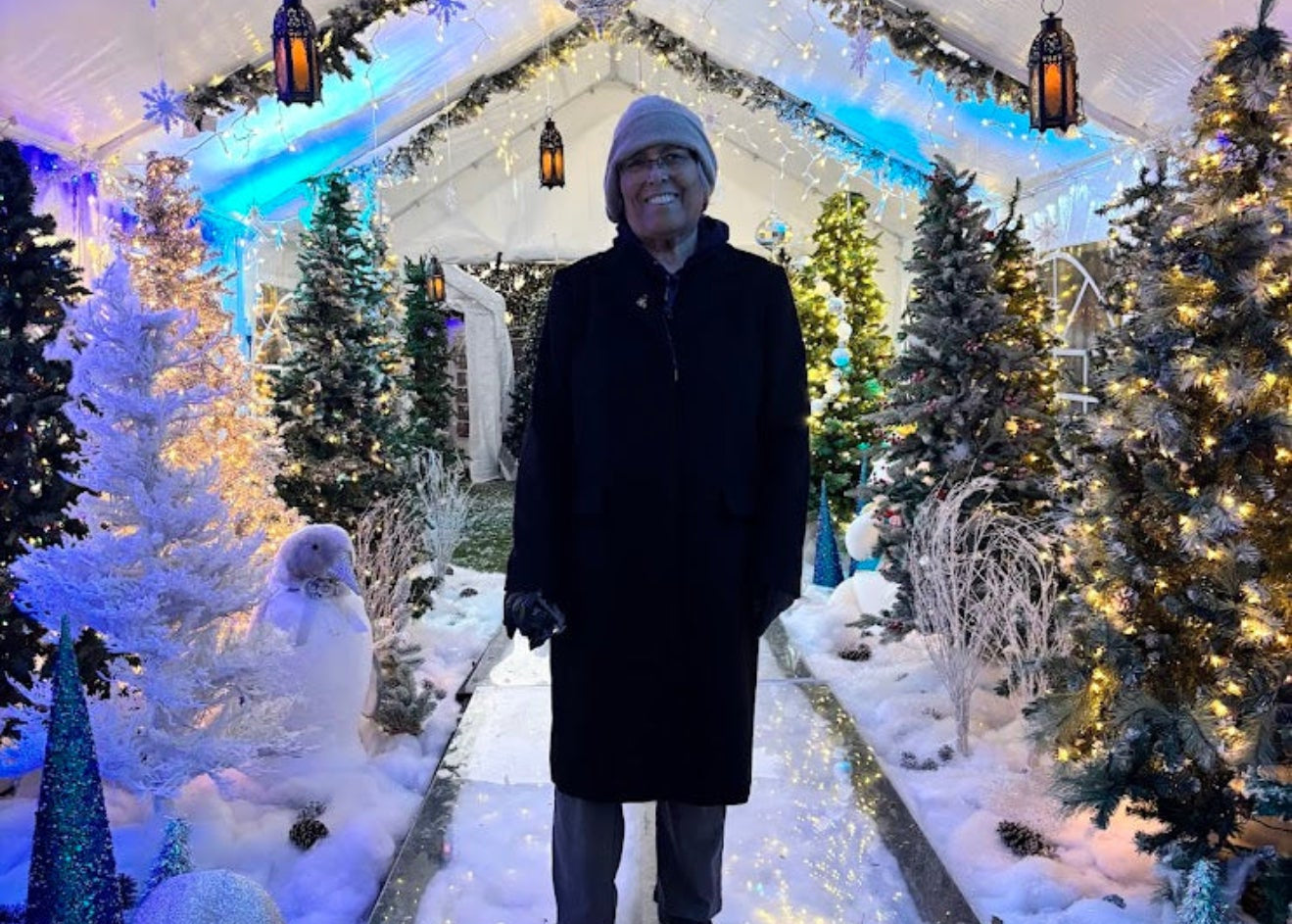 Person standing in a festive outdoor setting with Christmas decorations and a snowman.